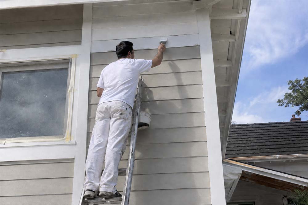 Male house painter on a ladder painting exterior weatherboards for a painter SEO services page.