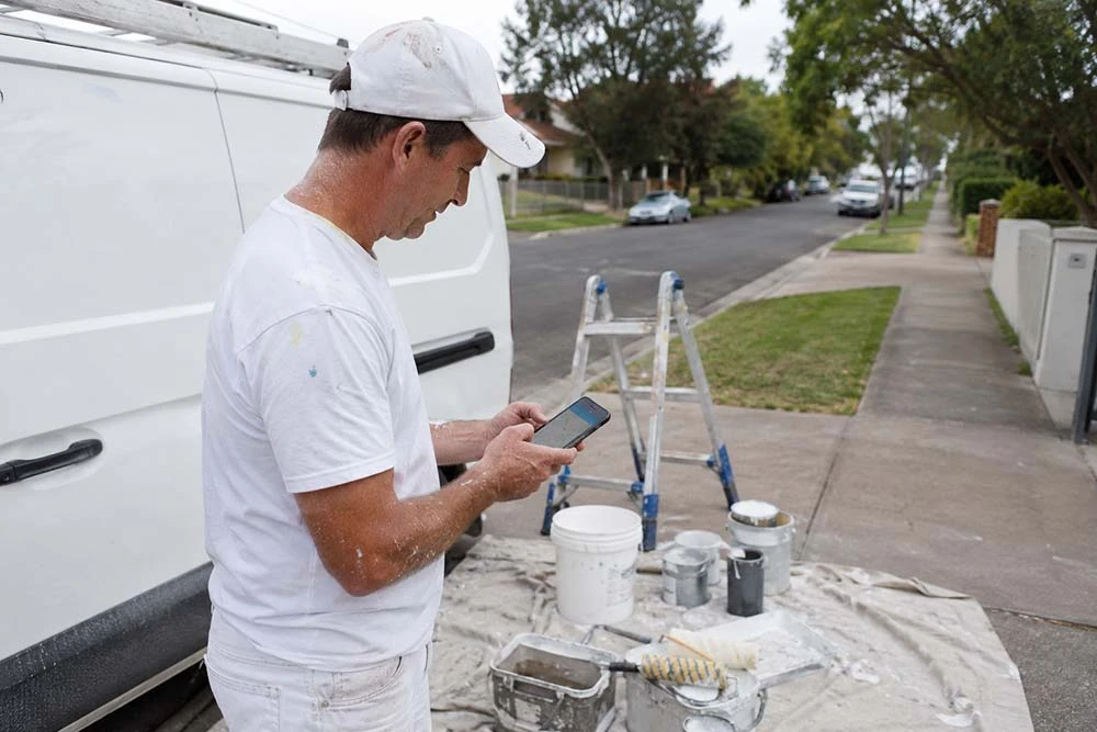 Painting contractor checking a local map on a phone near a work vehicle