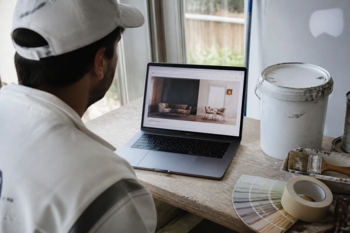 Painter reviewing a website on laptop beside paint equipment