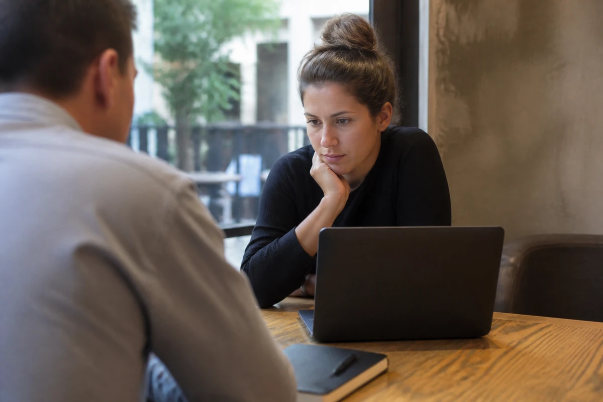 Sydney small business owner looking at a laptop with the while a consultant points at a closed notebook